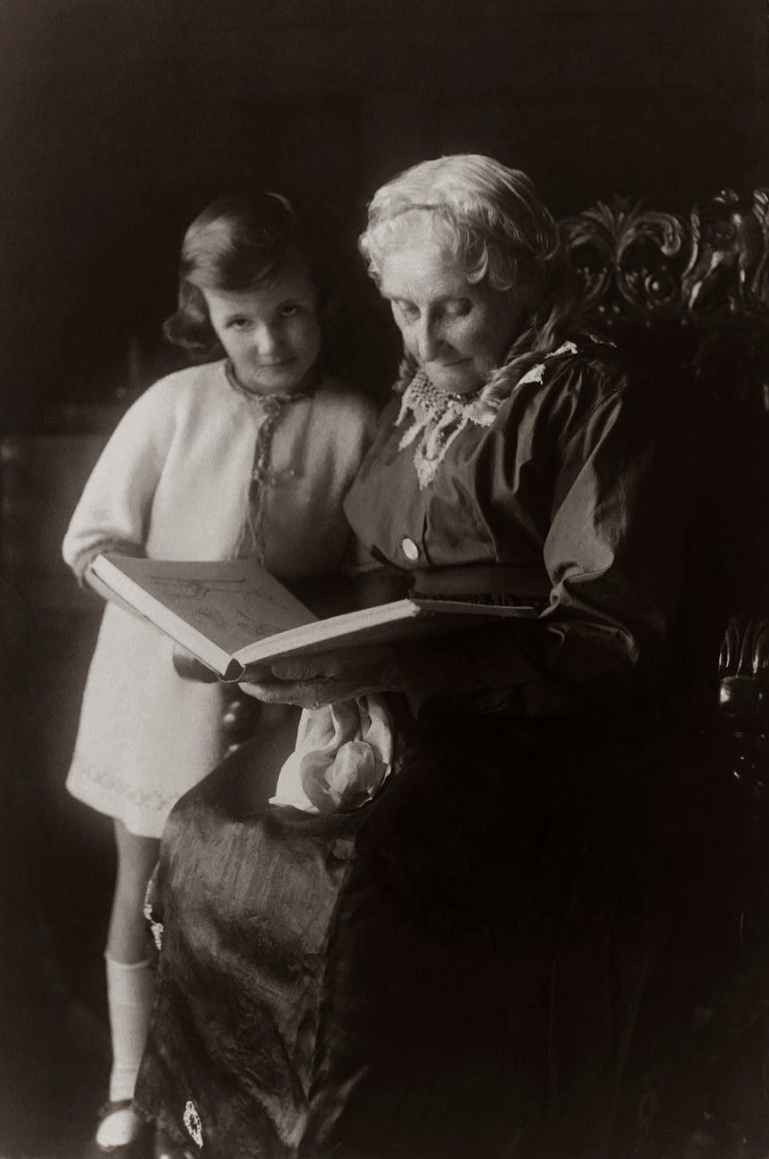 old woman sitting on chair near girl while reading a book