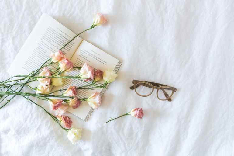 white and pink flowerson a book beside eyeglasses