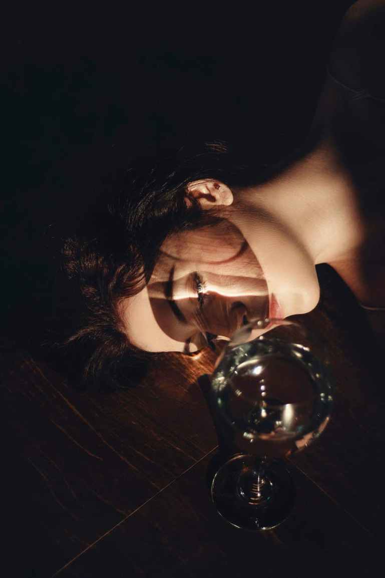 photo of woman lying beside a long stem clear wine glass