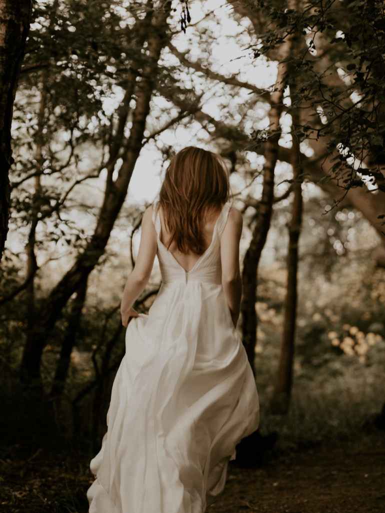 back view photo of woman in white dress walking in the woods