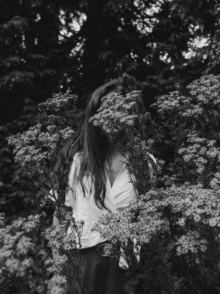 grayscale photography of woman standing near plants and trees