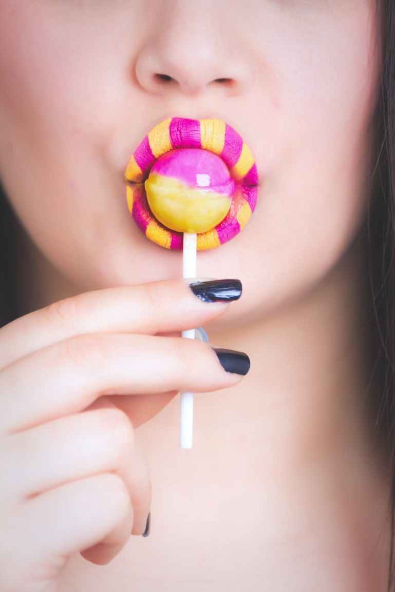 woman eating pink and yellow lollipop