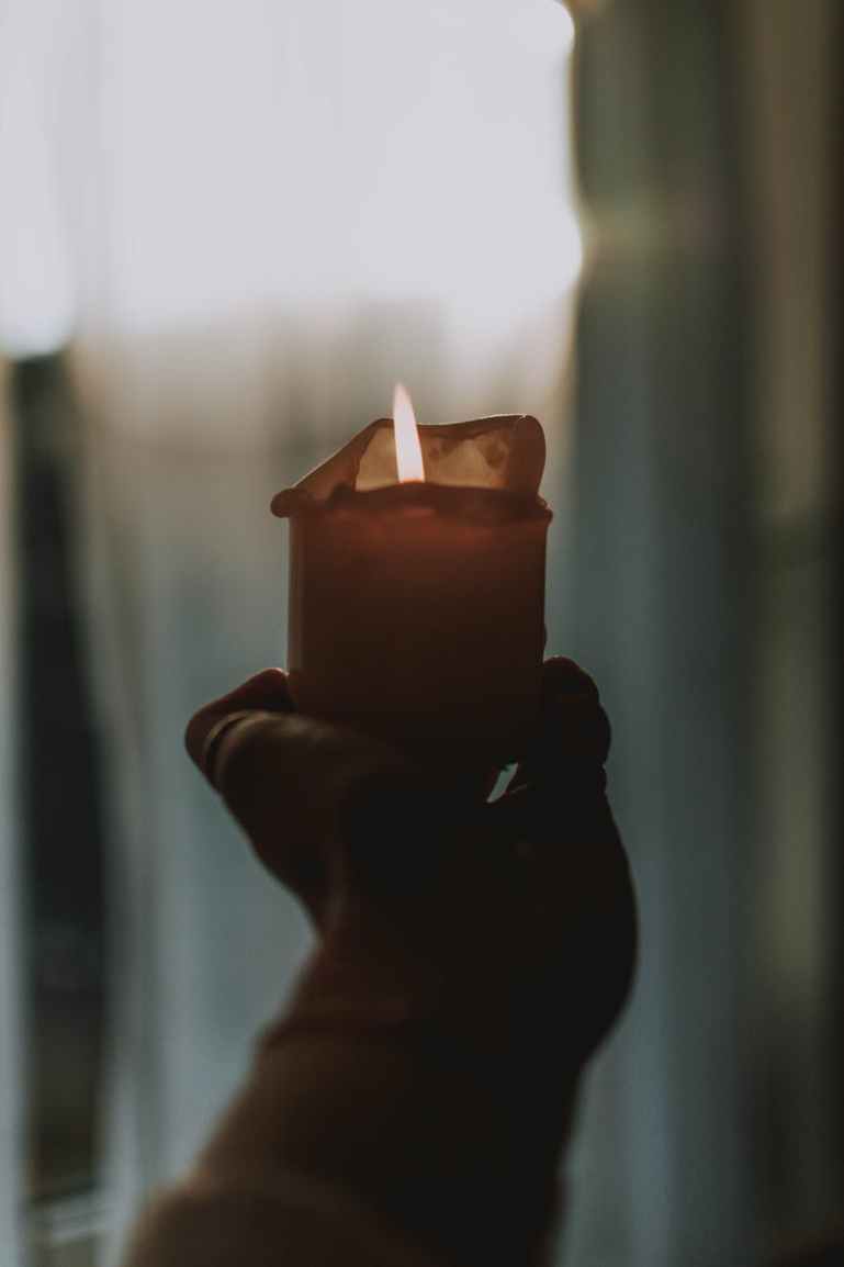 person holding lighted candle in dark room